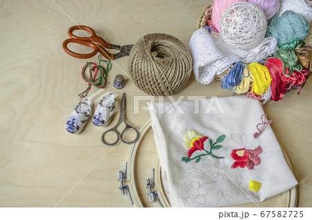 Light wooden table with frame, scissors, colored threads and needles necessary tools for decorative embroidery Light wooden table with frame, scissors, colored threads and needles necessary tools for decorative embroidery 67582725
