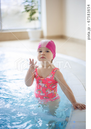 little girl in a pool cap and pink swimsuit learns to swim in the pool little girl in a pool cap and pink swimsuit learns to swim in the pool 67583654
