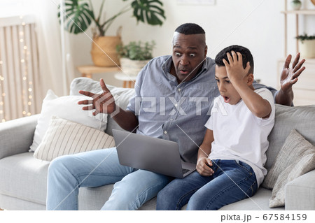 Computer Problem. Shocked Black Boy And His Grandfather Looking At Laptop Screen Computer Problem. Shocked Black Boy And His Grandfather Looking At Laptop Screen 67584159