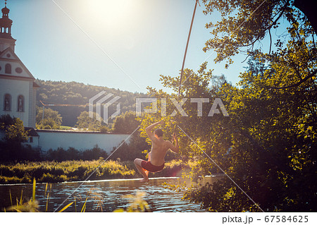 Man swinging on a rope into the water of a river 67584625