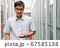 Handsome asian boy smiling and checking his smartphone in the hallway.  67585138