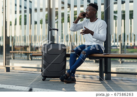 Young handsome Caucasian man in hat with backpack talking with smile on cellphone. Smiling cheerfully at train station. Attractive male traveller speaking on mobile phone at bus stop. Telephone call. Young handsome Caucasian man in hat with backpack talking with smile on cellphone. Smiling cheerfully at train station. Attractive male traveller speaking on mobile phone at bus stop. Telephone call. 67586263