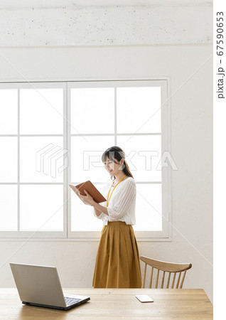 窓際で寄りかかって手帳を見る女性 67590653