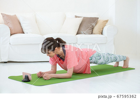 スマホを見ながら自宅でトレーニングをする若い女性 オンラインフィットネス スマホを見ながら自宅でトレーニングをする若い女性 オンラインフィットネス 67595362