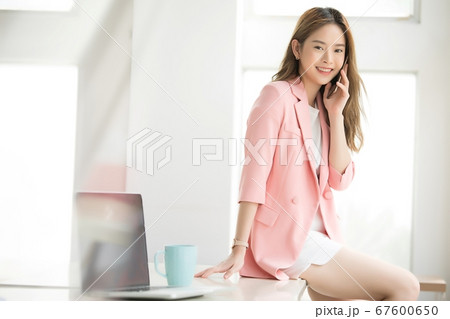 若い　若い　女性　会社員　ビジネス　オフィス　携帯　電話　デスク　座る　スタイル　人物　素材 67600650