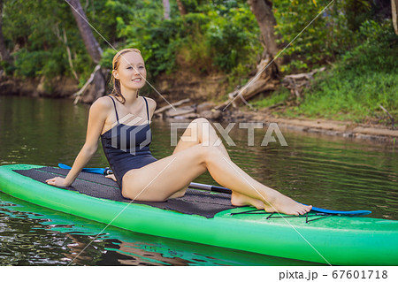Side view picture of a woman sitting and relaxing on the sup board. Surfer woman resting Side view picture of a woman sitting and relaxing on the sup board. Surfer woman resting 67601718