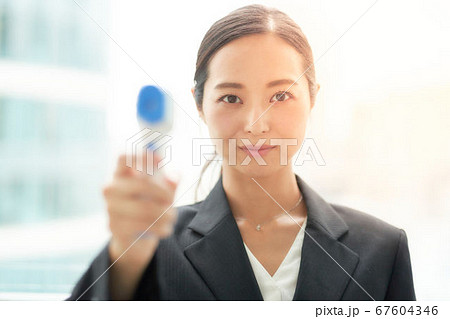 非接触体温計で検温をする女性 67604346