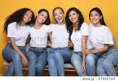 Cheerful Girls Friends Hugging Sitting On Bench On Yellow Background Cheerful Girls Friends Hugging Sitting On Bench On Yellow Background 67604593