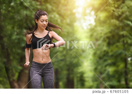 Trail Running Concept. Young man jogging and looking at his smart wrist watch, copy space, outdoor Trail Running Concept. Young man jogging and looking at his smart wrist watch, copy space, outdoor 67605105
