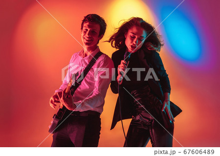 Young caucasian musicians, female singer and guitarist performing on gradient background in neon light. Concept of music, hobby, festival Young caucasian musicians, female singer and guitarist performing on gradient background in neon light. Concept of music, hobby, festival 67606489