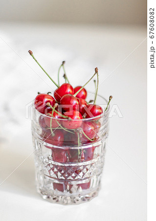 Close-up of glass bowl with ripe cherries stands on a white background with copy space, vertical photo Close-up of glass bowl with ripe cherries stands on a white background with copy space, vertical photo 67608082