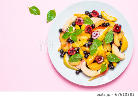 Fruit salad with berries in white plate, pink background Fruit salad with berries in white plate, pink background 67610383