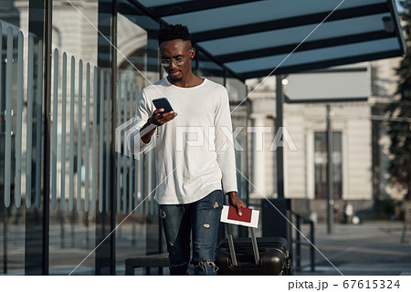 Young handsome Caucasian man in hat with backpack talking with smile on cellphone. Smiling cheerfully at train station. Attractive male traveller speaking on mobile phone at bus stop. Telephone call. Young handsome Caucasian man in hat with backpack talking with smile on cellphone. Smiling cheerfully at train station. Attractive male traveller speaking on mobile phone at bus stop. Telephone call. 67615324