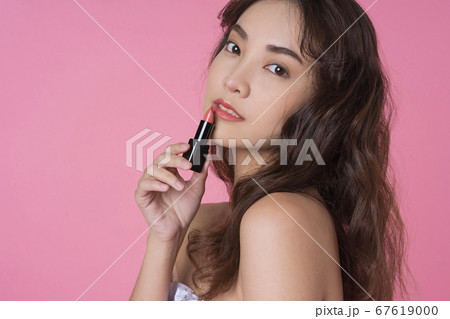 ピンク色背景で化粧品コスメを宣伝する美人女性モデルの写真素材