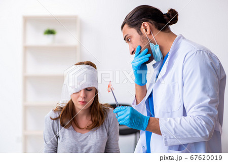Young head injured woman visiting young male doctor Young head injured woman visiting young male doctor 67620019
