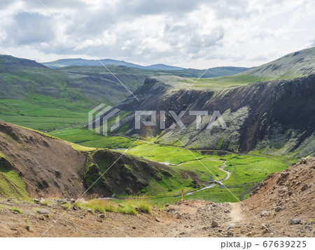 Reykjadalur valley with hot springs river, lush green grass meadow, rocks and hills with geothermal steam. South Iceland near Hveragerdi city. Summer sunny morning, blue sky. Reykjadalur valley with hot springs river, lush green grass meadow, rocks and hills with geothermal steam. South Iceland near Hveragerdi city. Summer sunny morning, blue sky. 67639225