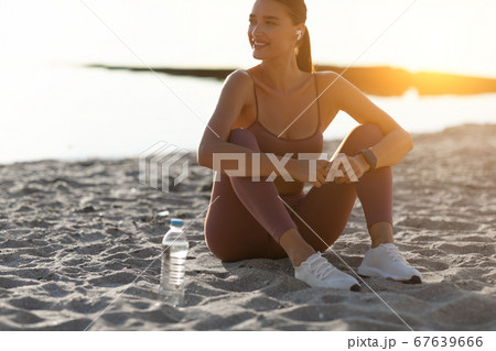 Happy healthy runner sitting on sand, listening to music 67639666