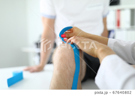 Knee joint of kinesiotape is fixed to patient in medical office. 67640802