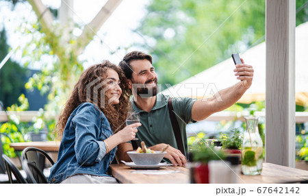 Happy couple sitting outdoors on terrace restaurant, taking selfie. 67642142