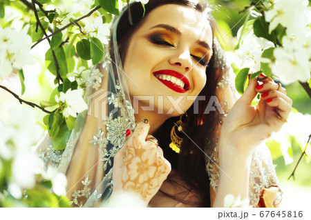 young pretty indian girl in jewelry and veil posing cheerful happy smiling in green park, lifestyle people concept 67645816