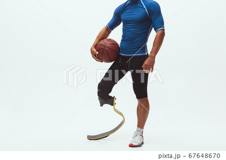 Athlete with disabilities or amputee isolated on white studio background. Professional male basketball player with leg prosthesis training and practicing in studio. Athlete with disabilities or amputee isolated on white studio background. Professional male basketball player with leg prosthesis training and practicing in studio. 67648670