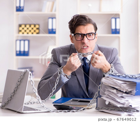 Busy employee chained to his office desk Busy employee chained to his office desk 67649012