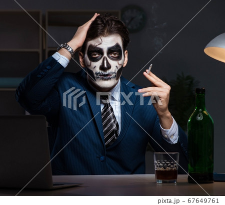Businessman with scary face mask working late in office Businessman with scary face mask working late in office 67649761