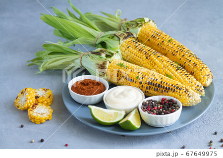 Plate of fried grilled young sweet corn cobs with spices, lime and souce. Summer food concept Plate of fried grilled young sweet corn cobs with spices, lime and souce. Summer food concept 67649975