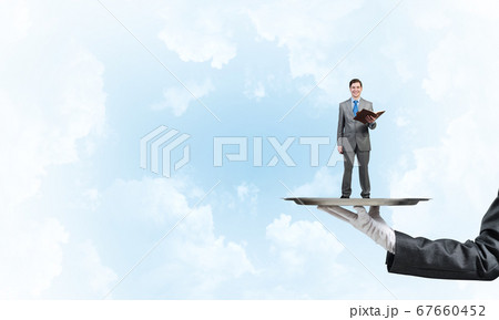 Businessman on metal tray with red book in hands against blue sky background 67660452