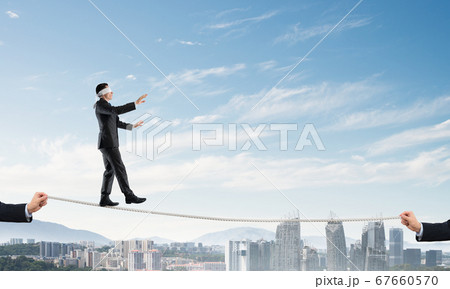 Business concept of risk support and assistance with man balancing on rope Business concept of risk support and assistance with man balancing on rope 67660570