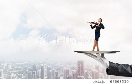 Attractive businesswoman on metal tray playing violin aginst cityscape background 67663530