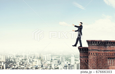 Danger and risk concept with businessman making step from edge Danger and risk concept with businessman making step from edge 67666303