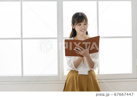 窓際で皮の手帳を見る若い女性 67667447
