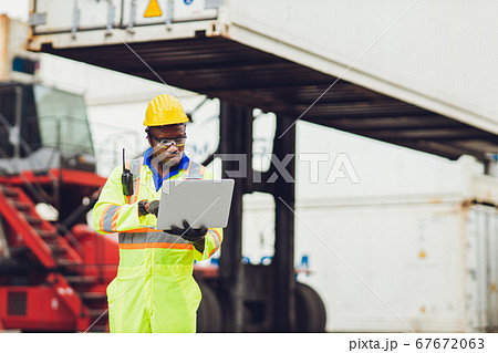 Black African worker working in logistic shipping using laptop to control loading containers 67672063