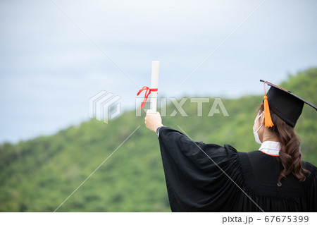 Graduated woman wear cap gown and Medical mask for protection virus holding diploma or certificated due Virus outbrake and COVID-19 virus flu pandemic,New normal of graduation day Graduated woman wear cap gown and Medical mask for protection virus holding diploma or certificated due Virus outbrake and COVID-19 virus flu pandemic,New normal of graduation day 67675399