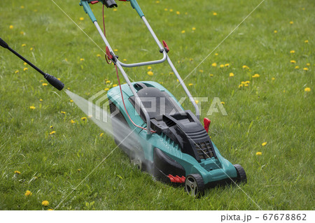 high-pressure washer washes lawn mower with jet of water on green grass high-pressure washer washes lawn mower with jet of water on green grass 67678862
