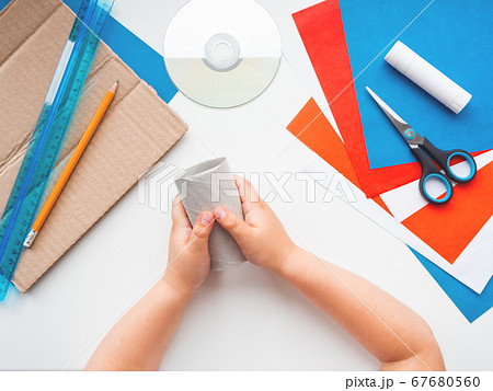 Child makes eco-friendly toy of colored paper and used toilet paper core. Also he needs carton, scissors, glue, CD-disk, pencil and ruler. Reuse tissue rolls. Making toys from improvised materials. 67680560