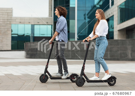 Couple riding motorized kick scooters in the city 67680967