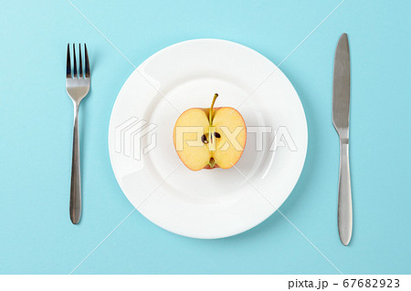 Half of ripe juicy apple on a white dinner plate, table knife and fork on a blue background. 67682923