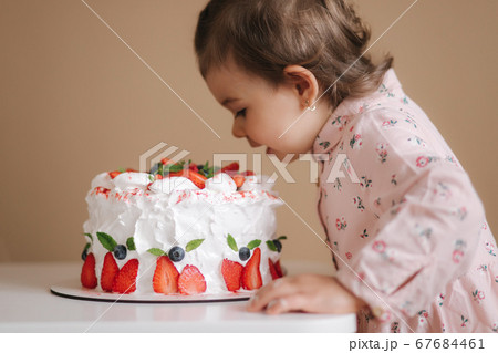 Little girl first time taste bithday cake. Cute little girl in beautiful dress tasting cake with strawberries Little girl first time taste bithday cake. Cute little girl in beautiful dress tasting cake with strawberries 67684461