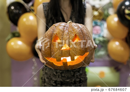 Young adult woman hold in hand spooky custom weird handmade orange pumpkin head with carved faces and glowing candle or light inside. Halloween party decoration celebrate traditional autumn holiday Young adult woman hold in hand spooky custom weird handmade orange pumpkin head with carved faces and glowing candle or light inside. Halloween party decoration celebrate traditional autumn holiday 67684607
