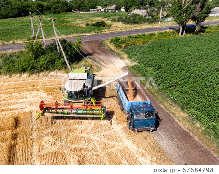 Aerial drone top view Big powerful industrial combine harvester machine unloading bin of wheat cereal field in truck on bright summer or day. Agricultural yellow field machinery landscape background 67684798