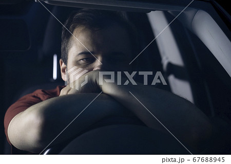 Young bearded man lies with his hands on the steering wheel of a car. Young bearded man lies with his hands on the steering wheel of a car. 67688945