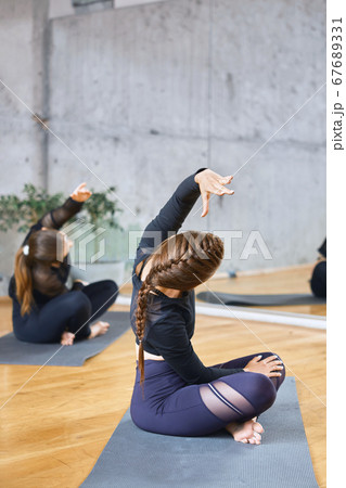 Women practicing practicing lotus pose in hall. 67689331