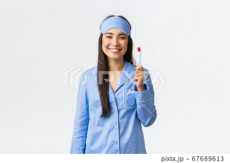 Hygiene, lifestyle and people at home concept. Cheerful smiling asian girl in pajamas and sleeping mask showing toothbrush and white perfect teeth, use whitening toothpaste, white background Hygiene, lifestyle and people at home concept. Cheerful smiling asian girl in pajamas and sleeping mask showing toothbrush and white perfect teeth, use whitening toothpaste, white background 67689613