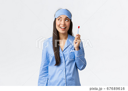 Hygiene and people at home concept. Girl have great idea while brushing her teeth in bathroom before going sleep. Asian female in pajamas and sleeping mask holding toothbrush and look amazed 67689616