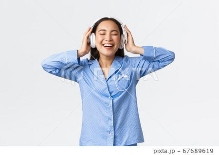 Home leisure, weekends and lifestyle concept. Happy pleased asian woman in pajamas enjoying awesome sound quality in new earphones, dancing in pajamas and listening music 67689619