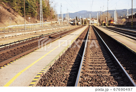 Empty train station in small city on sunny day, shallow depth of field photo, focus on concrete platform and steel rails foreground Empty train station in small city on sunny day, shallow depth of field photo, focus on concrete platform and steel rails foreground 67690497