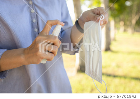 Hand of girl is holding a face mask,spraying alcohol on medical mask,clean washing for reuse,disinfecting mask using spray alcohol cleaning after their use during the Coronavirus,Covid-19 pandemic Hand of girl is holding a face mask,spraying alcohol on medical mask,clean washing for reuse,disinfecting mask using spray alcohol cleaning after their use during the Coronavirus,Covid-19 pandemic 67701942