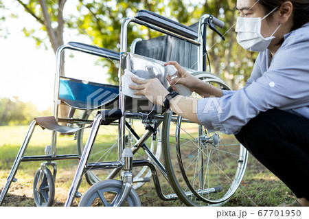 Woman is spraying alcohol and wiping the dirt and dust,disinfectant spray on wheelchair at nursing home,prevention of contagious disease of Covid-19,Coronavirus,wipe cleaning,disinfecting wheelchair 67701950